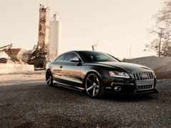 arafed black audi припаркован перед фабрикой с силосом на заднем плане