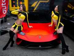 две женщины в желтых и черных нарядах стоят рядом с красным спорткаром