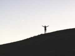 человек стоит на холме с поднятыми руками