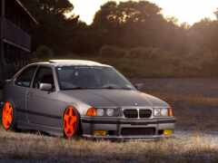 bmw e36 купе с оранжевыми ободками припарковано в поле