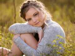 женщина, сидящая в поле высокой травы с руками, сложенными над коленями