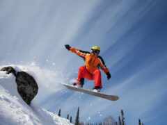 лыжник в оранжевых прыжках делает прыжок на заснеженную гору