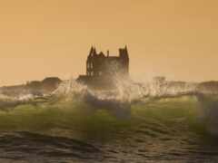 серферы катаются на волнах перед замком