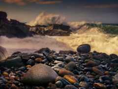 камни и галька на пляже с волной, разбивающейся на заднем плане