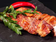 есть кусок мяса на черной тарелке с красным перцем