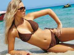 блондинка в бикини лежит на пляже с лодкой на заднем плане