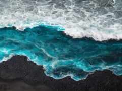 вид с воздуха на волну, разбивающуюся на пляже с человеком на доске для серфинга