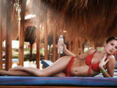 женщина в красном бикини лежит на синем коврике с бутылкой воды