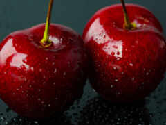 две красные вишни, сидящие на черной поверхности с каплями воды