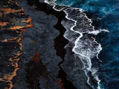 вид с воздуха на пляж с волной, разбивающейся о скалы