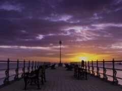 фиолетовый и желтый закат над пирсом со скамейками и фонарным столбом