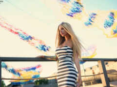 блондинка в полосатом платье, стоящая на перилах с воздушными змеями на заднем плане