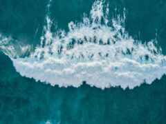 вид с воздуха на волну, разбивающуюся о океан с серфером на переднем плане