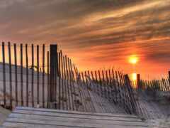 закат над забором и песчаными дюнами со скамейкой на переднем плане