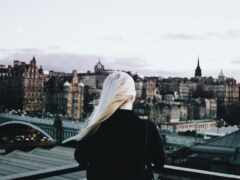 блондинка с длинными волосами смотрит на городской горизонт с крыши