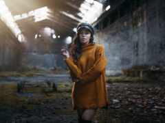 женщина в желтом пальто и шляпе, стоящая в заброшенном здании