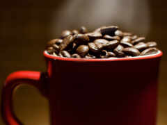 на столе красная чашка, наполненная кофейными зернами