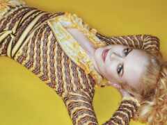 блондинка, лежащая на желтой поверхности с желтым и черным узорным платьем