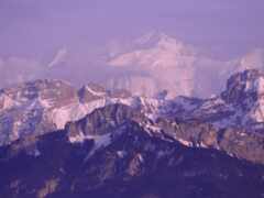 горы, покрытые снегом и облаками с самолетом, летящим в небе