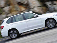 arafed white bmw suv едет по дороге возле каменной стены