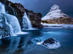 водопад посреди замерзшего озера с горой на заднем плане