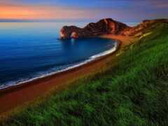 травянистый холм с видом на океан с пляжем и скальным образованием