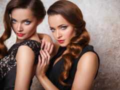 две женщины в черных платьях позируют для фото с руками на плечах