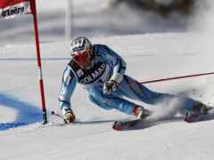 лыжник в сине-белом костюме катается по склону возле красного флага