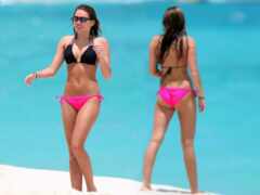 женщина в розовом бикини гуляет по пляжу с подругой