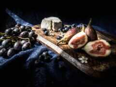 есть разделочная доска с виноградом, инжиром и сыром на ней