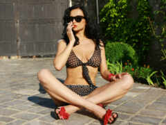 женщина, сидящая на кирпичном патио и разговаривающая по мобильному телефону во время ношения бикини