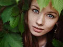 есть женщина, которая смотрит в камеру сквозь листья
