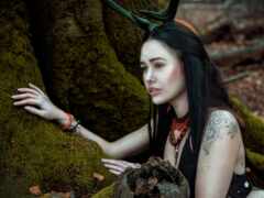 женщина с рогами и красным ожерельем, сидящая перед деревом