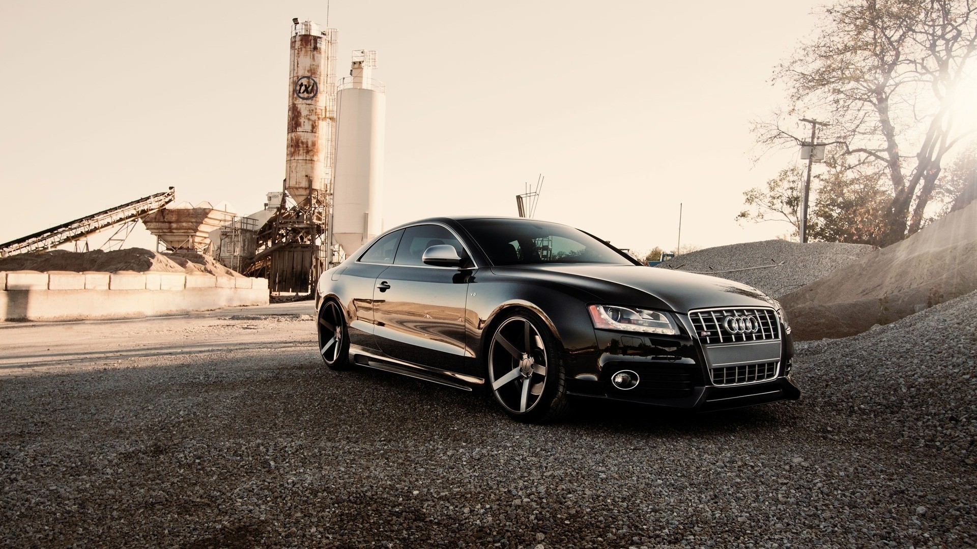 arafed black audi припаркован перед фабрикой с силосом на заднем плане