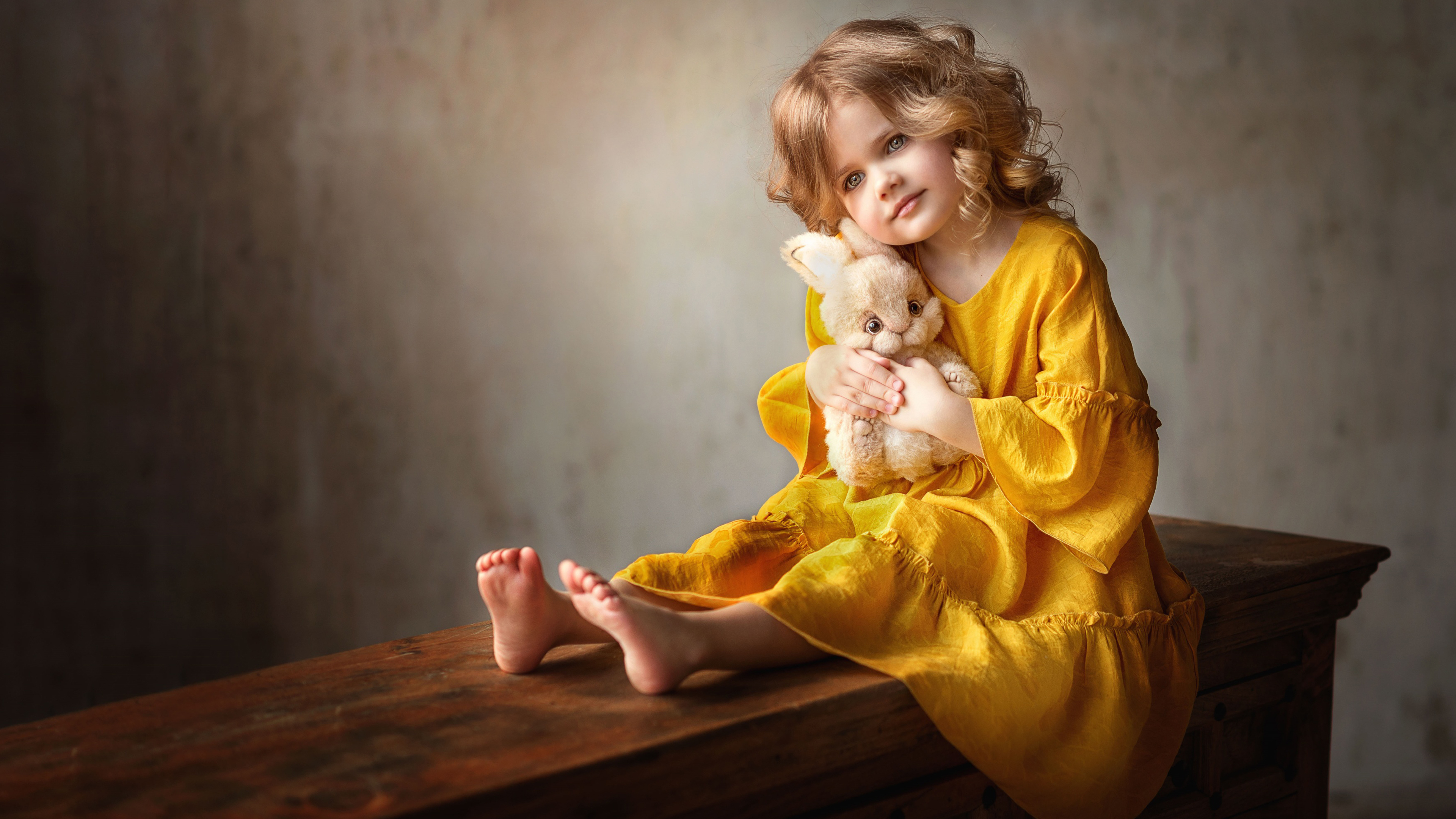 маленькая девочка сидит на скамейке, держа плюшевого медведя