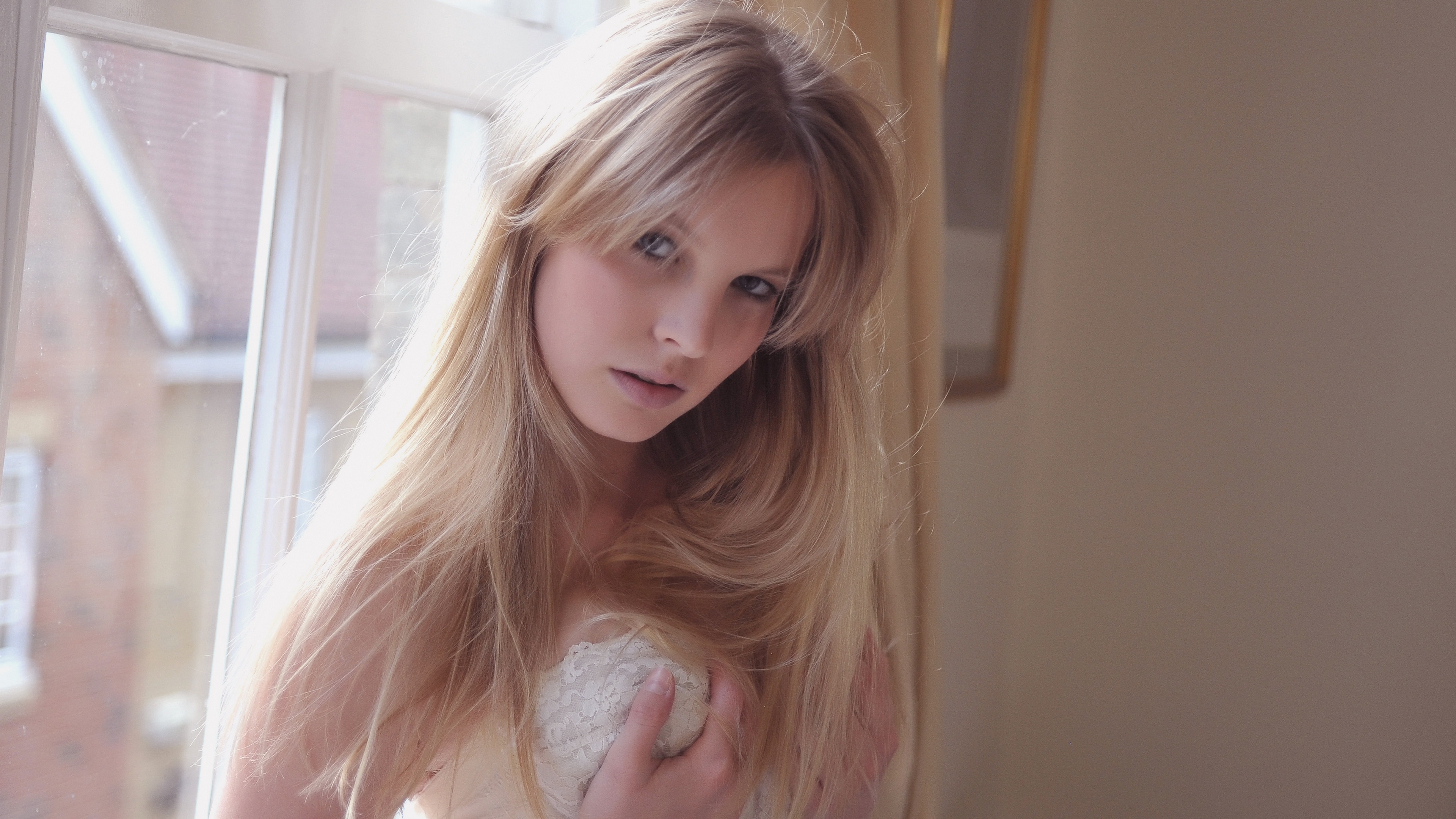 блондинка с длинными волосами держит плюшевого медведя перед окном