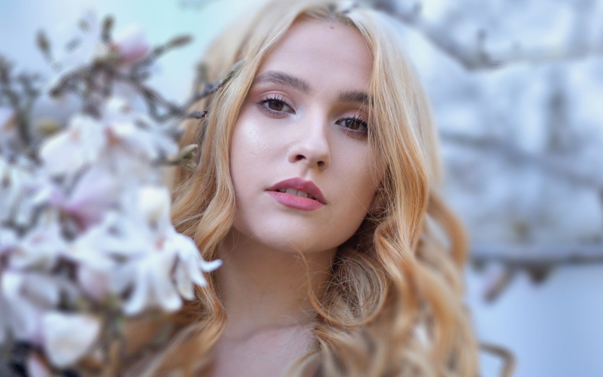 блондинка с длинными волосами и голубыми глазами, стоящая перед деревом