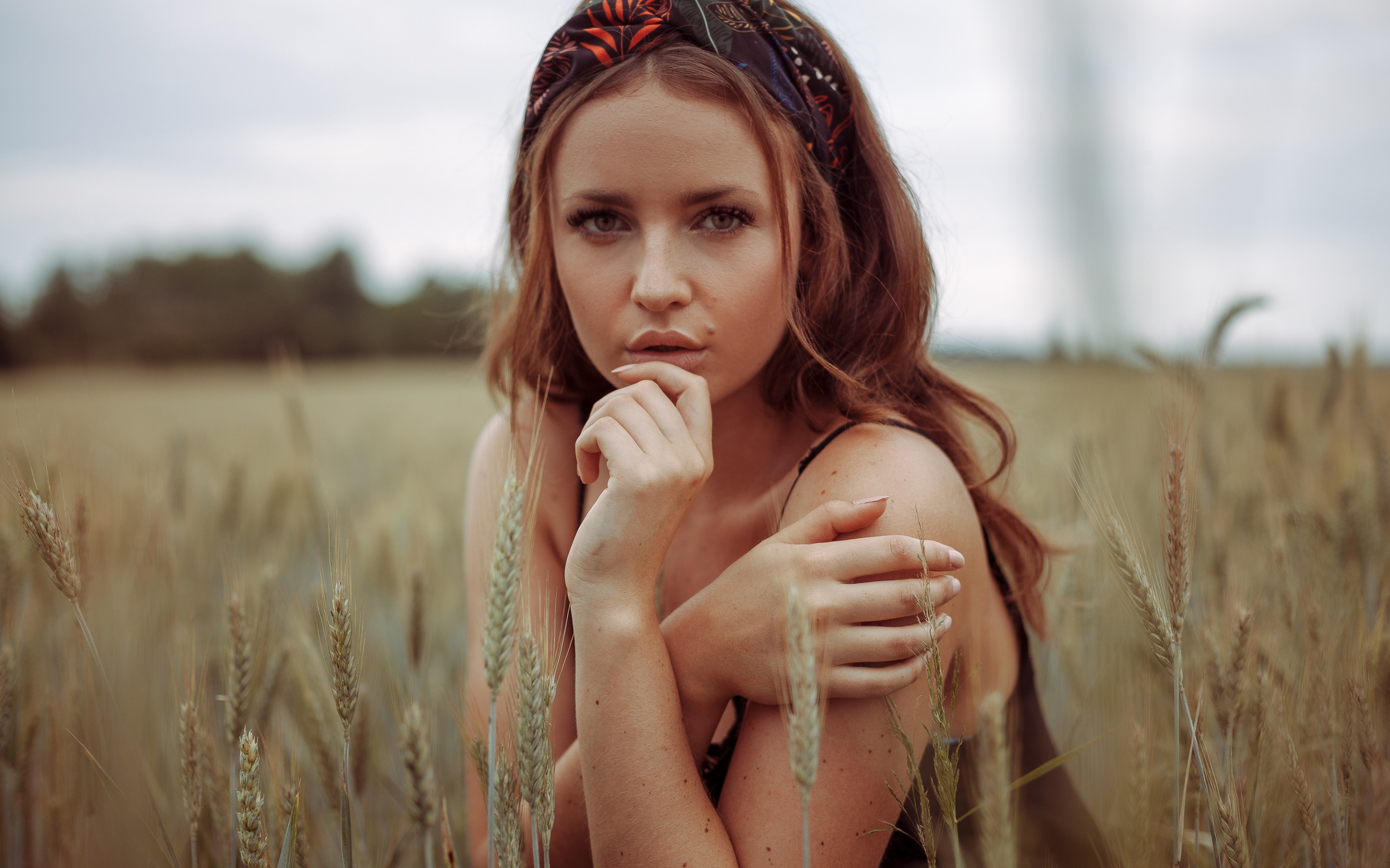 женщина на пшеничном поле с рукой на подбородке