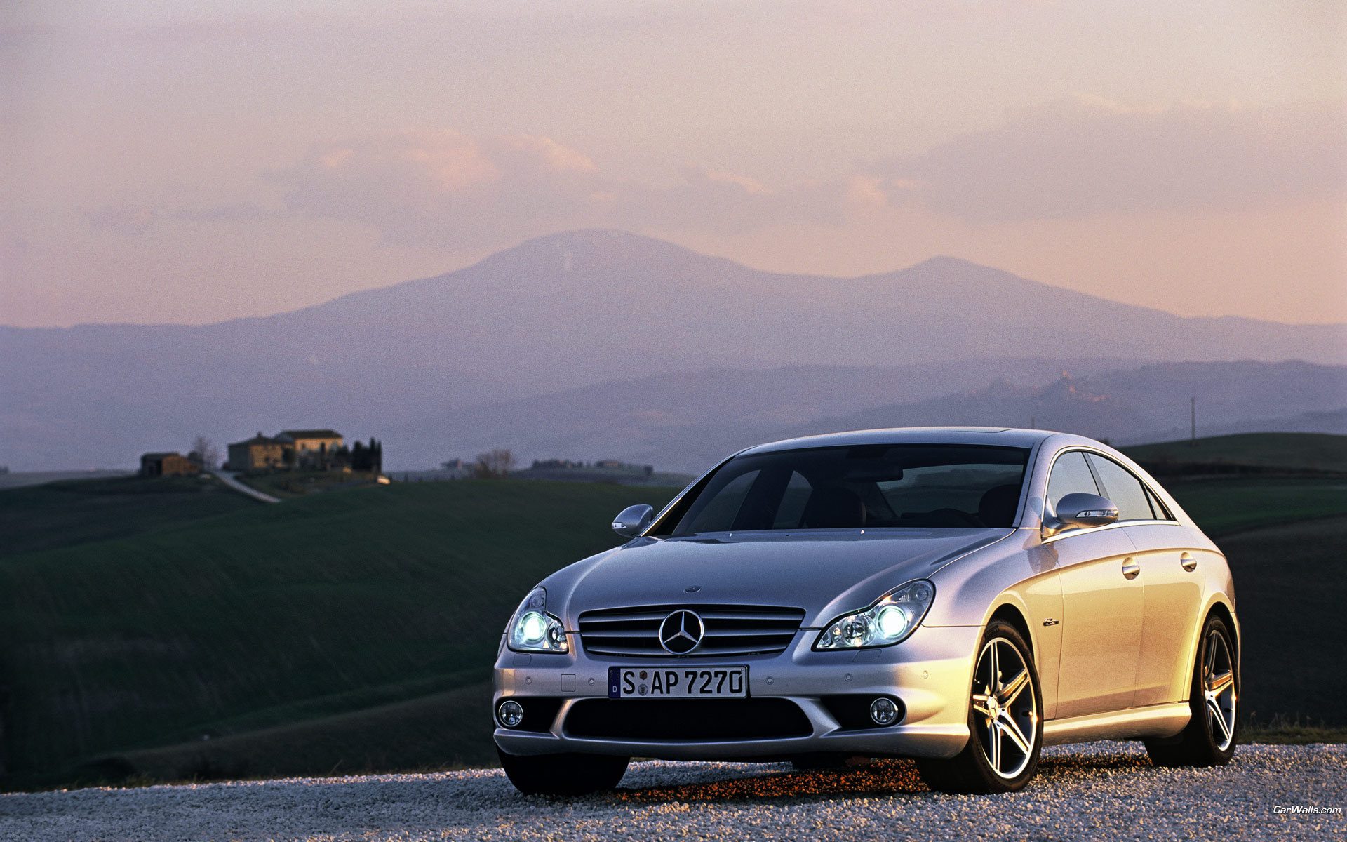 серебряный автомобиль, припаркованный на гравийной дороге с горами на заднем плане