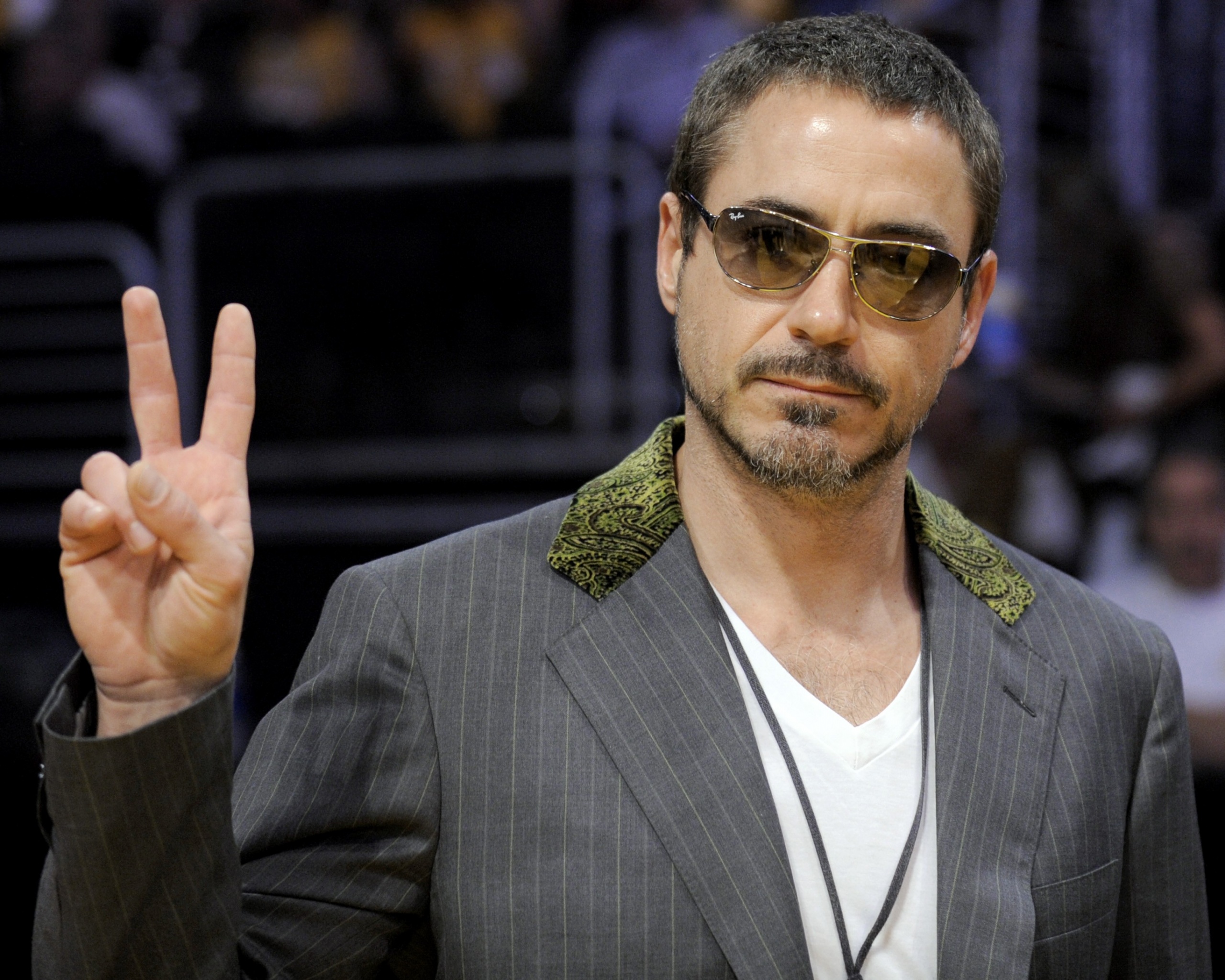 женщина в костюме и солнцезащитных очках делает знак мира