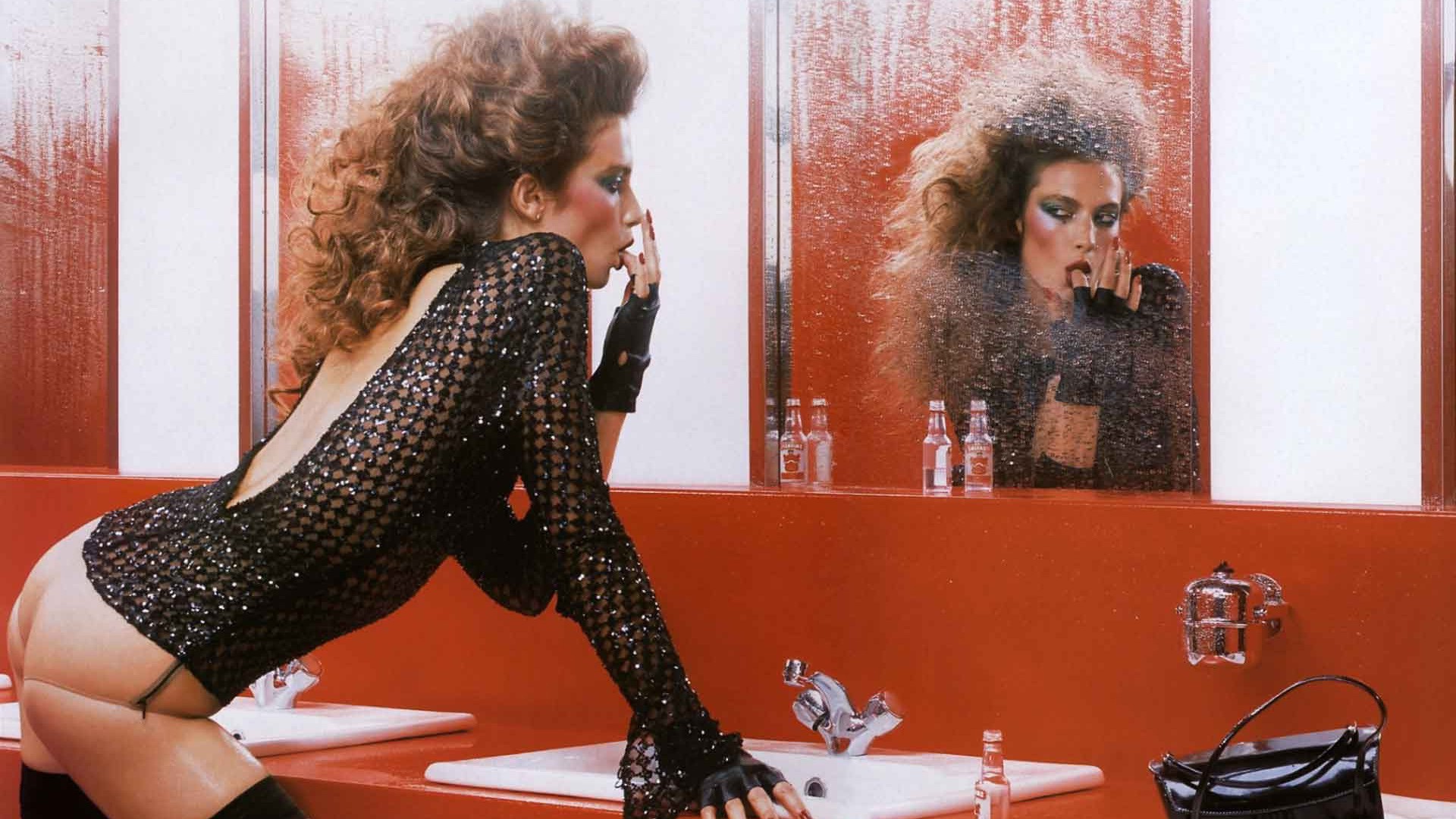 женщина в черном платье стоит перед зеркалом