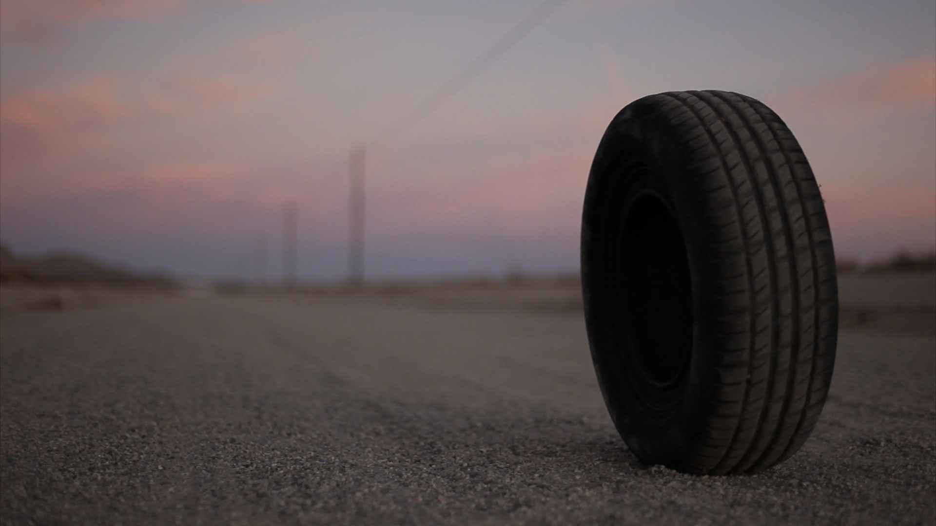 шина на земле посреди пустыни с розовым небом на заднем плане