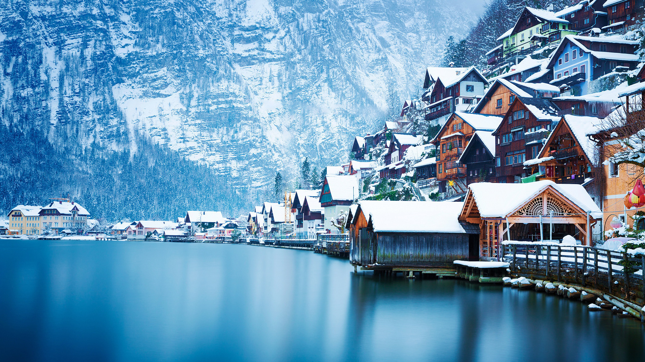 снежные горы окружают озеро и ряд домов