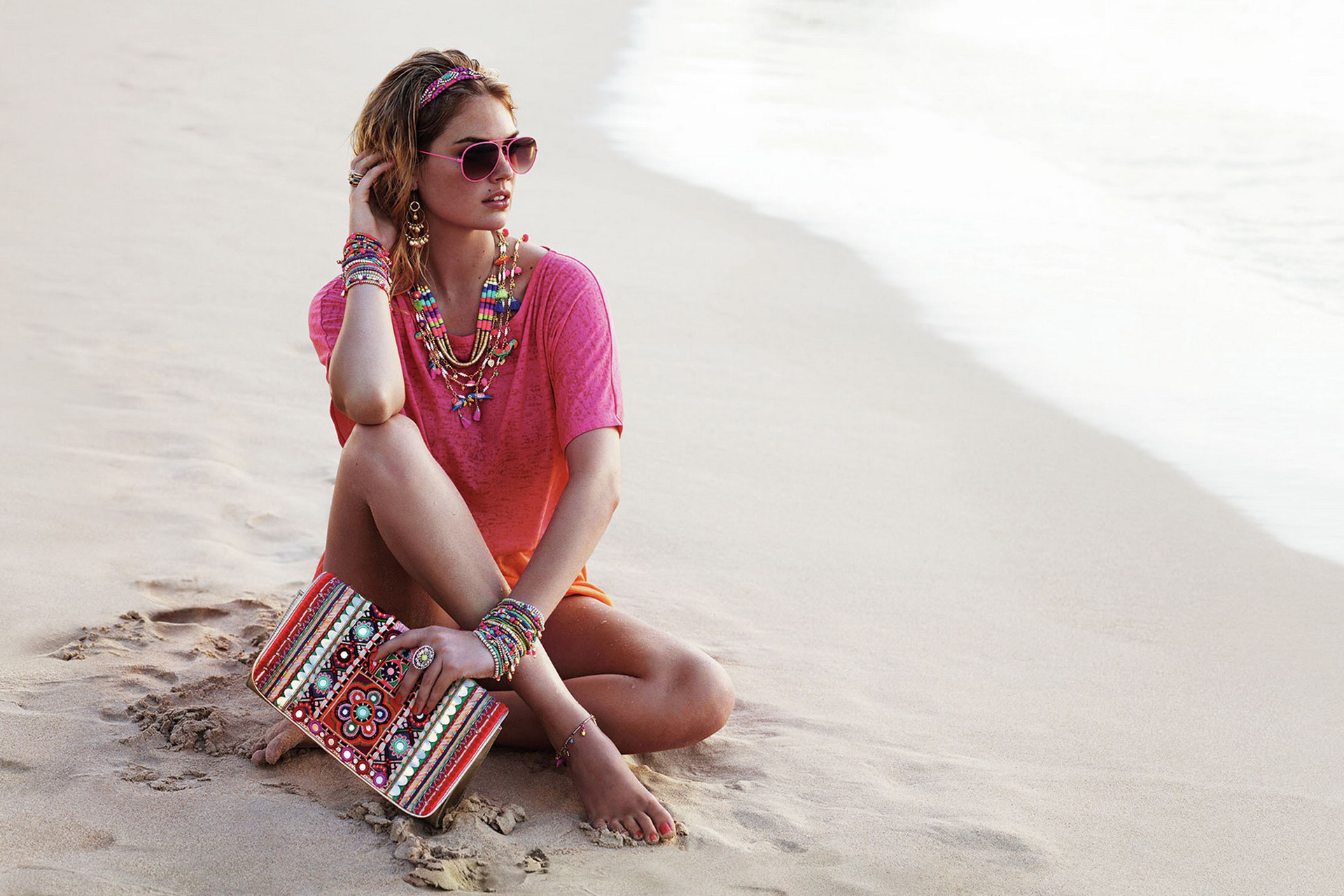 женщина, сидящая на пляже с кошельком и солнцезащитными очками