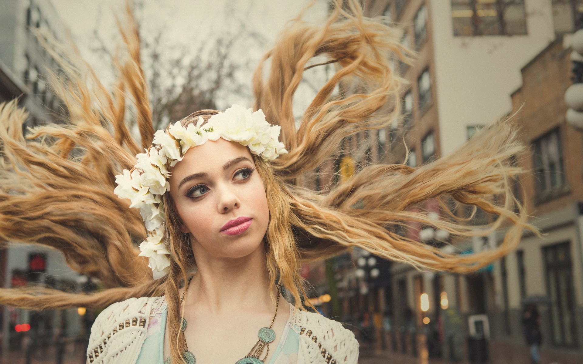 блондинка с цветочной короной на городской улице со зданиями на заднем плане